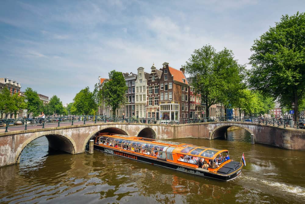 Amsterdam, Netherlands -  Orange boat of the Lovers Canal Cruises with tourists boating through the famous Keizersgracht canal intersection in Amsterdam
