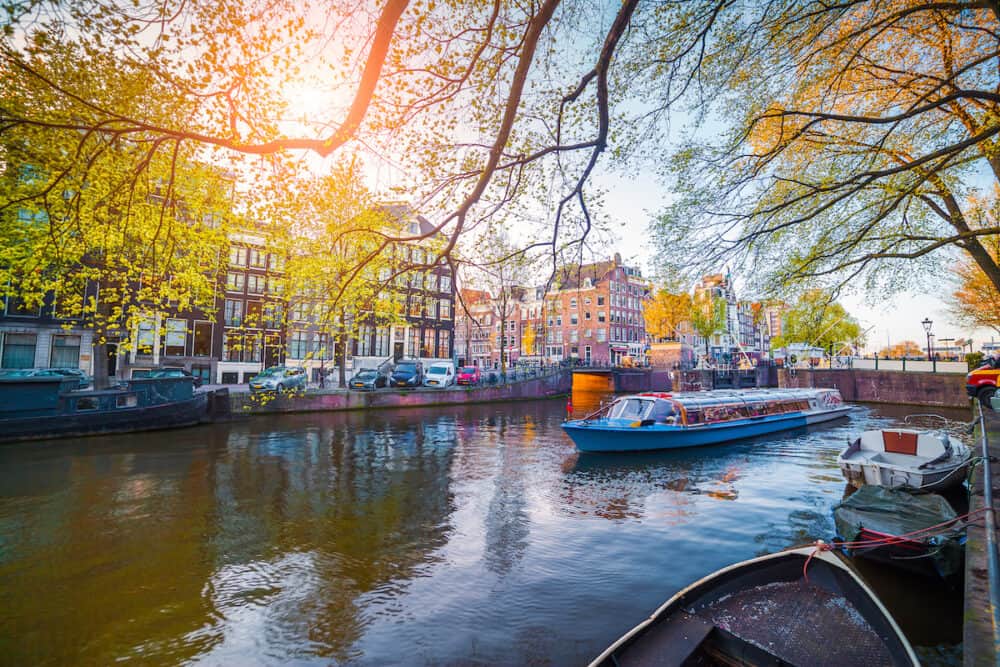 Spring scene in Amsterdam city. Tours by boat on the famous Dutch canals. Colorful evening landscape in Netherlands Europe.