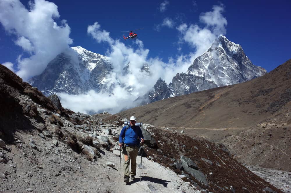 Everest trek, Hiker walking on trail and helicopter flying at Thokla Pass (4830 m) with view of Tabuche Peak and Arakam Tse in Himalayas mountains, Sagarmatha national park, Solukhumbu, Nepal