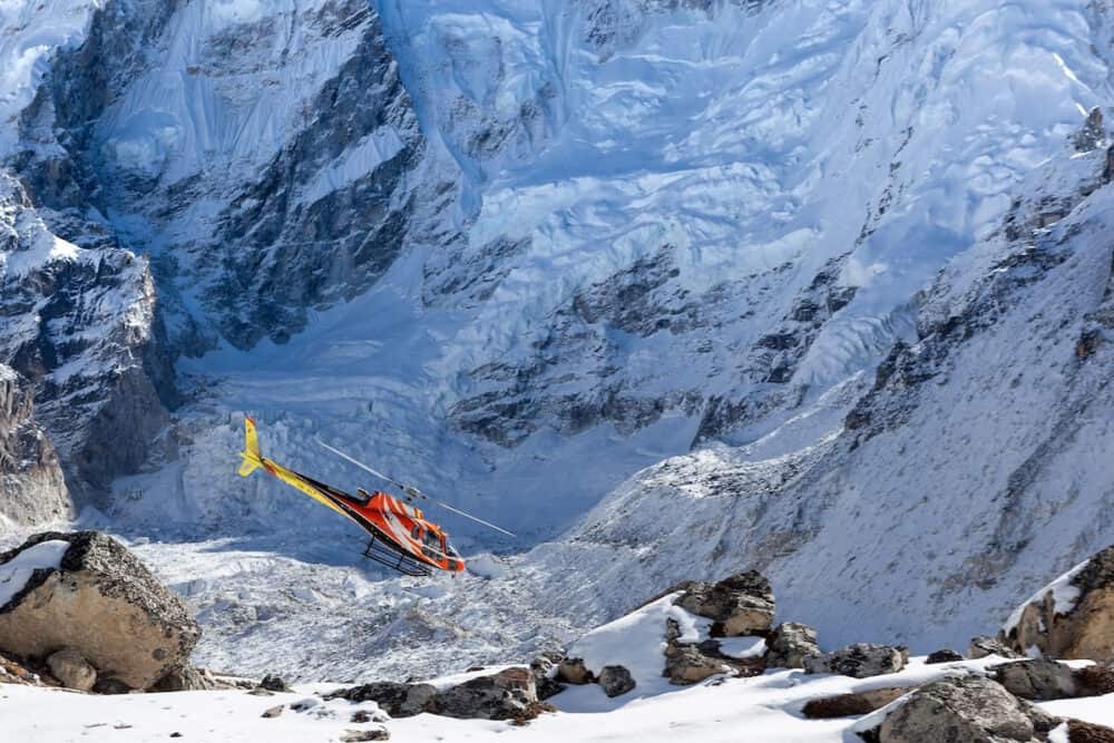 EVEREST BASE CAMP TREK/NEPAL - Rescue helicopter in high Himalayan mountains. Red rescue helicopter landing on snowy ground with vertical snowy mountain wall on the background.