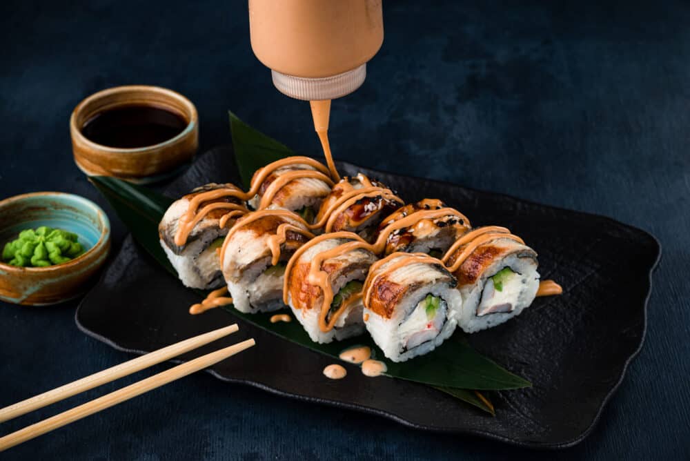 Close-up view of process of preparing rolling sushi. making the sushi with sauce and sesame seeds, pours delicious fresh rolls with a sauce. Dark background