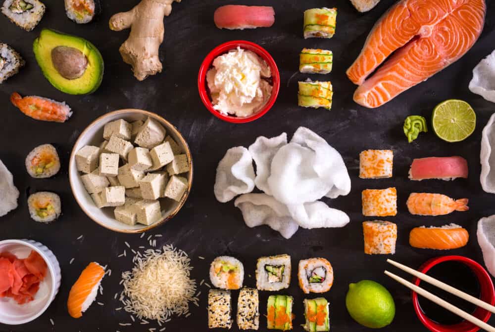 Set of traditional japanese food on a dark background. Sushi rolls nigiri raw salmon steak rice cream cheese avocado lime pickled ginger (gari) raw ginger wasabi soy sauce nori ?hopsticks. Asian food frame. Dinner party. Space for text