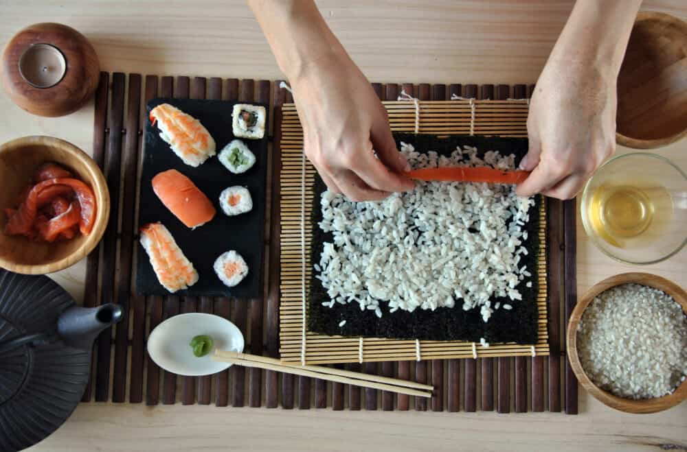 hands cooking sushi with rice salmon and nori