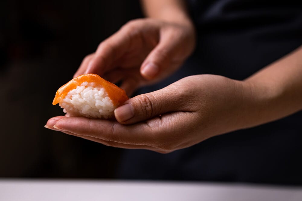Close-up of chef's hands preparing Japanese food. Japanese chef prepares sushi in a restaurant. A young chef prepares traditional Japanese sushi on a cutting board.