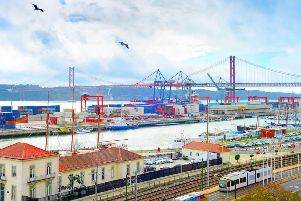 Seagulls over Lisbon commercial port, ships containers and freight cranes, skyline with Bridge and Tagus river, Portugal