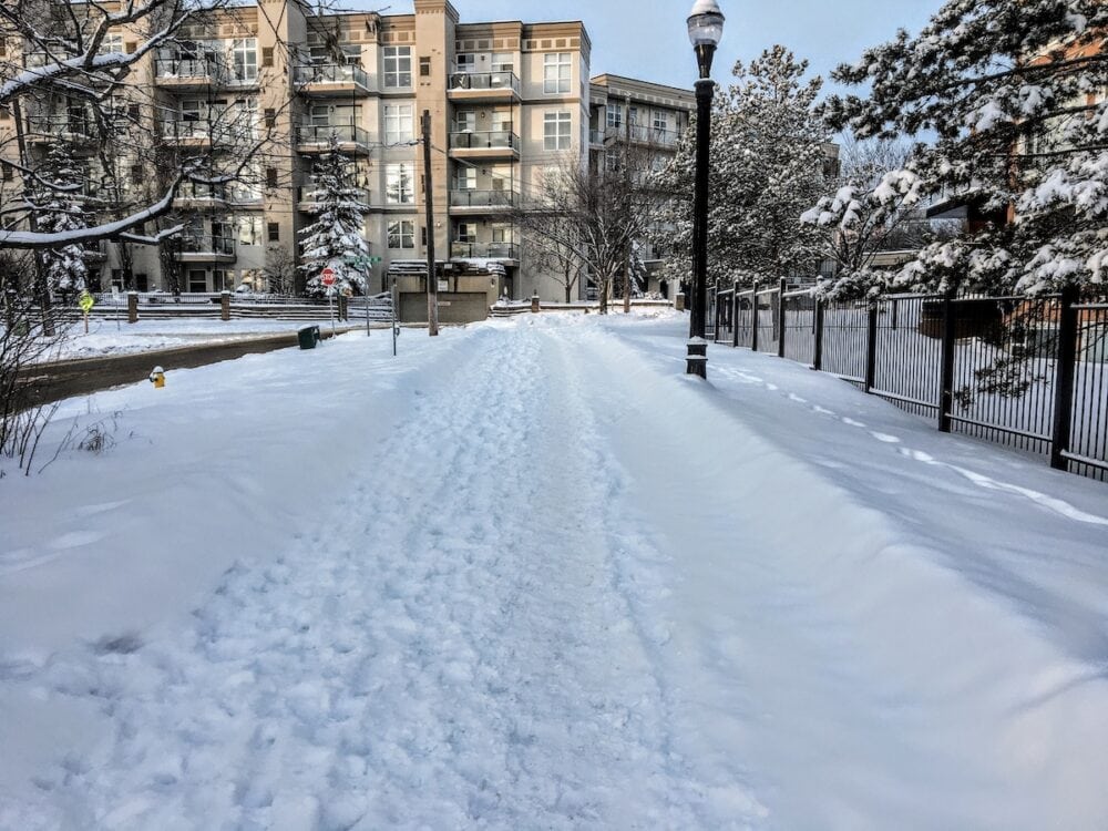 An empty sidewalk and street with old footprints in the snow as people now stay in their homes during the pandemic, in Edmonton, Alberta, Canada