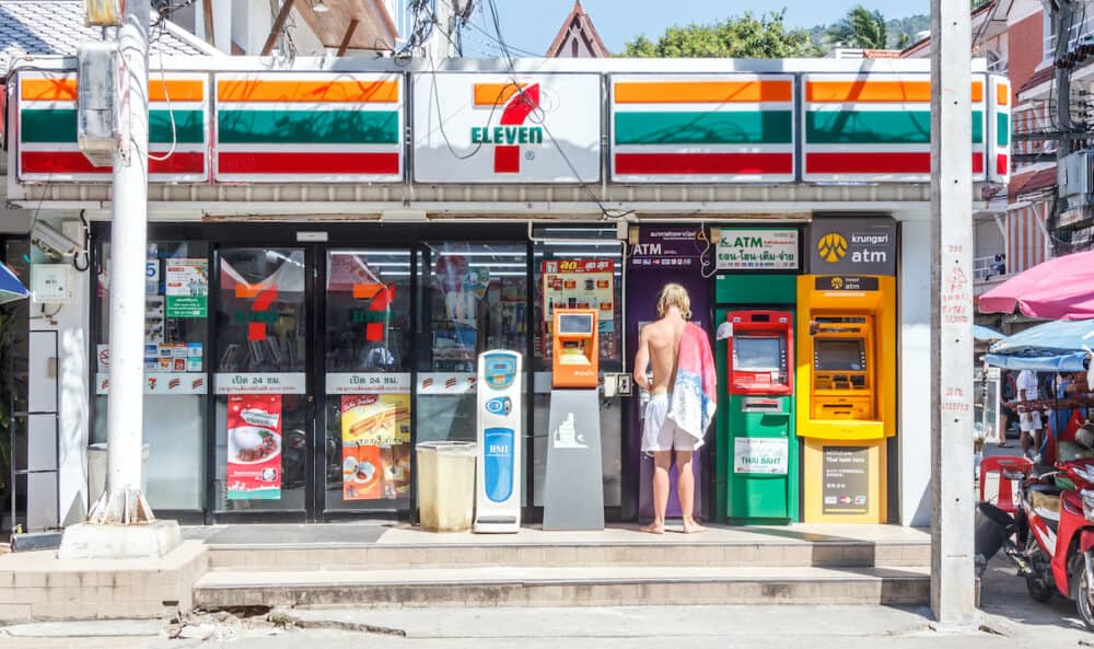 Phuket, Thailand - Tourist at ATM outside a 7 eleven shop in Patong. Convenience stores are everywhere.