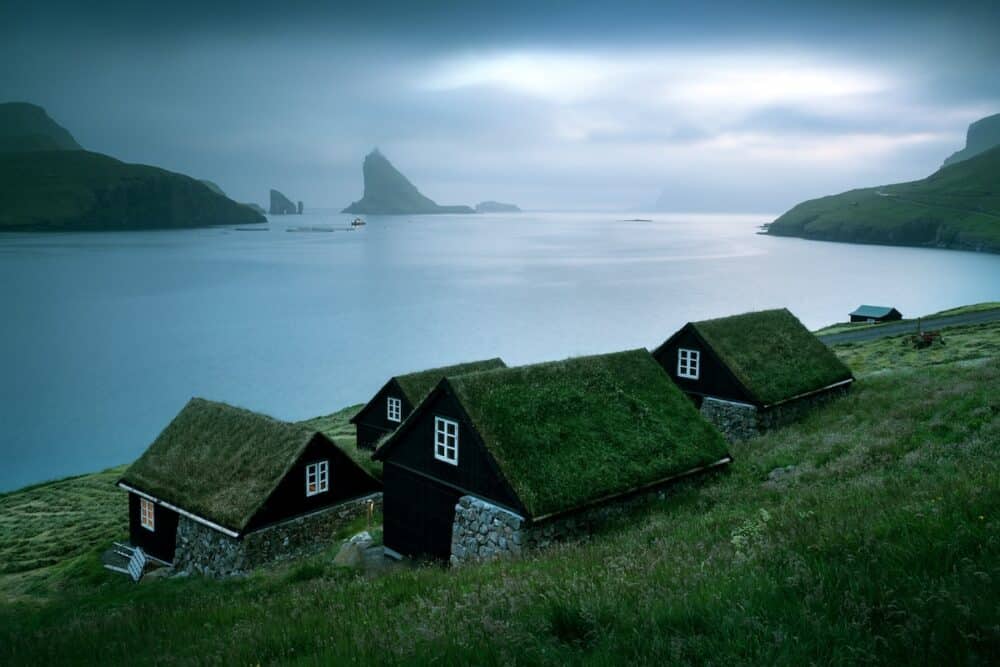 Picturesque view of traditional faroese grass-covered houses in the village Bour. Drangarnir and Tindholmur sea stacks on background. Vagar island, Faroe Islands, Denmark. Landscape photography