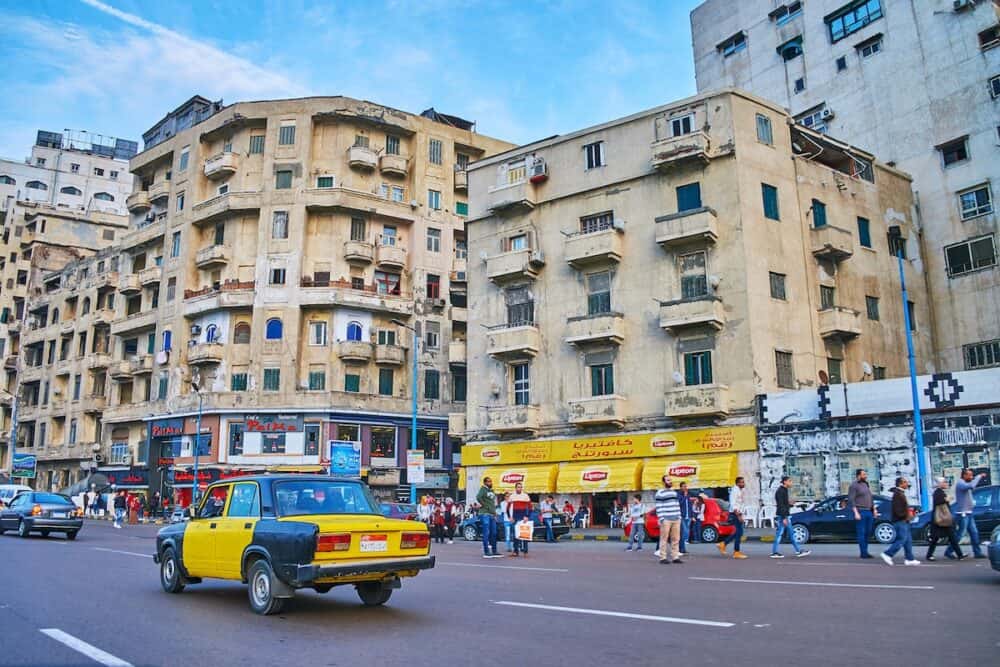 ALEXANDRIA, EGYPT - The black-yellow taxi rides along El-Gaish road with shabby housing on background