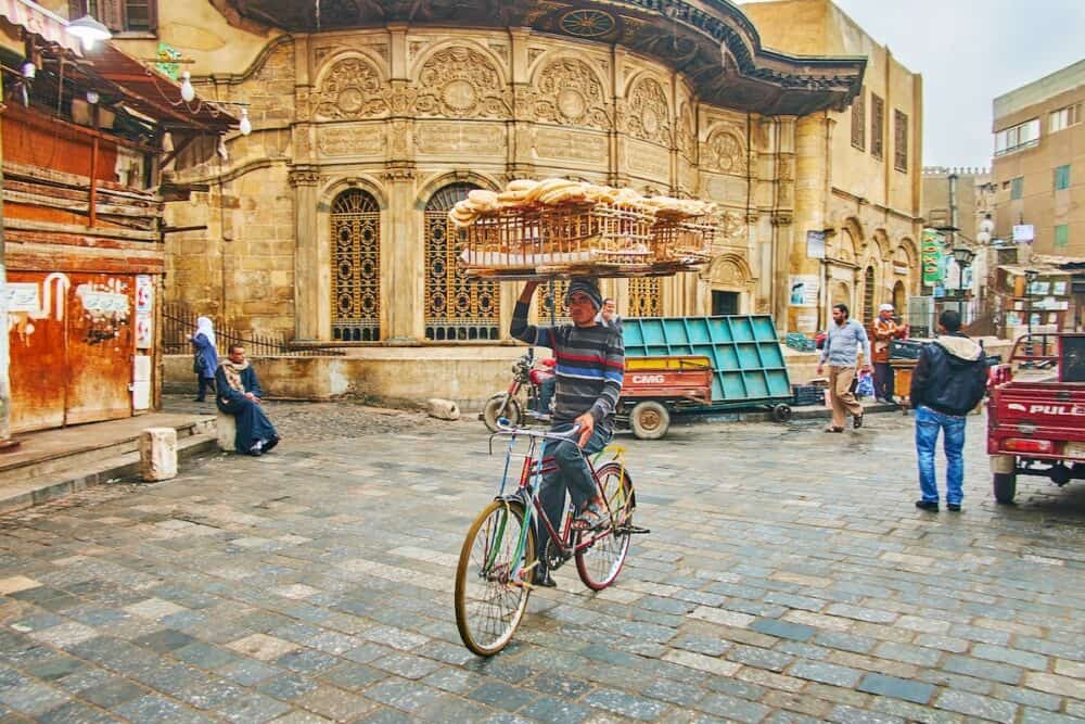 CAIRO, EGYPT - Traditional bread delivery in old town - the cyclist with large wooden basket rides next to  Sabil wa Kuttab of Tusun Pasha in Al-Muizz street in Cairo.