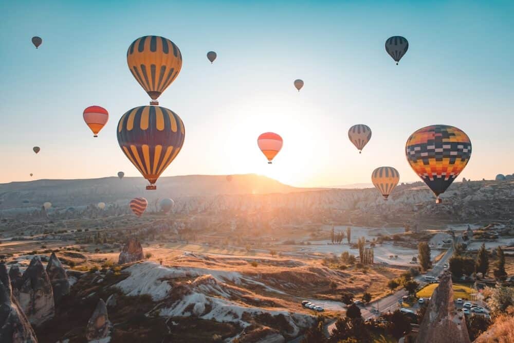 Cappadocia sunrise hot air balloons fly over Goreme valley landscape with stone caves. People in colorful hotair ballons enjoy wonderful dawn watching, aerial view. Tourism, travel holidays background