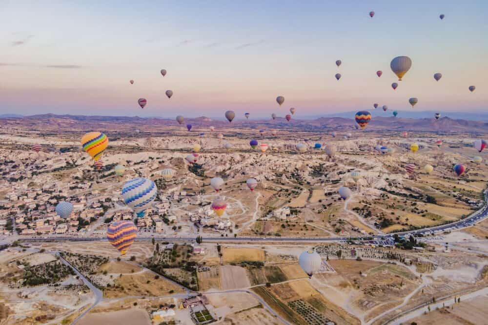 Colorful hot air balloons flying over at fairy chimneys valley in Nevsehir, Goreme, Cappadocia Turkey. Spectacular panoramic drone view of the underground city and ballooning tourism. 