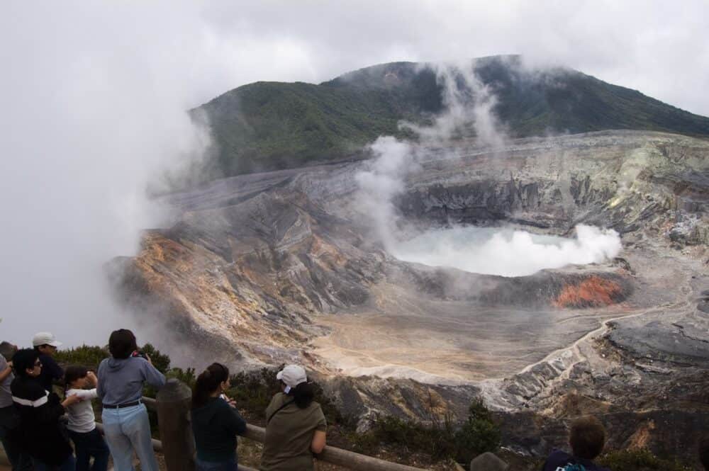 Aerial view of Poas Volcano. Group of tourists looking at its crater while smoke comes out.