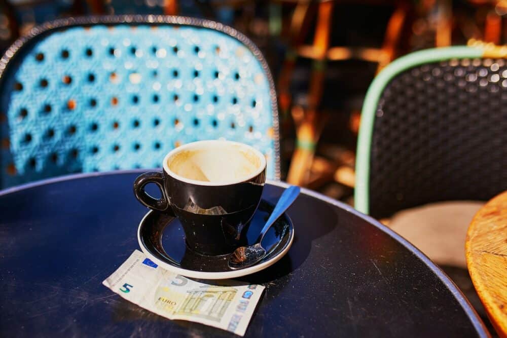 Empty cup of black coffee and 5 euro bank note on a table of outdoor cafe in Paris, France