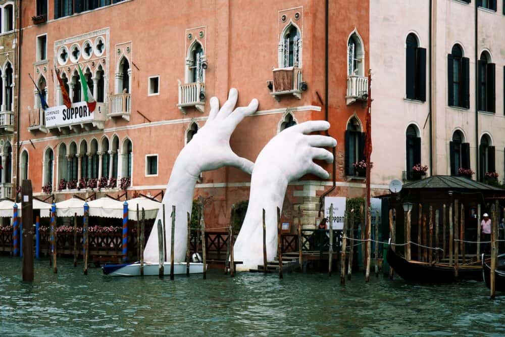 Support by Lorenzo Quinn. Gigantic hands rise from water to support the Ca' Sagredo Hotel, a statement of the impact of climate change and rising sea levels.