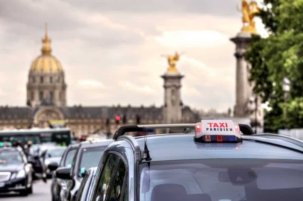 Parisian taxi illuminated sign on the car roof and Les Invalides on the background in Paris, France.