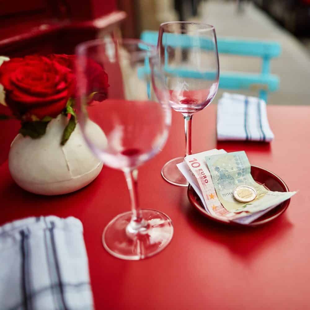 Two empty wine glasses and tip in an outdoor Parisian restaurant focus on money