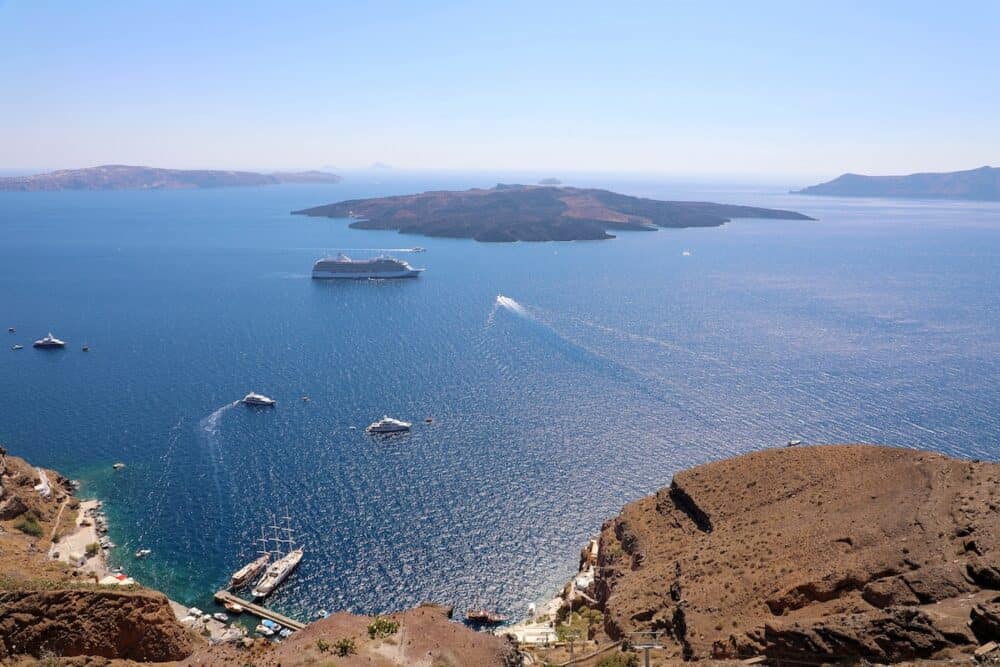 Beautiful panoramic view from touristic Fira town to caldera and volcano at summer sunny day. Santorini (Thira) island. Seascape. Picturesque natural background. Cyclades. Greece. Europe.