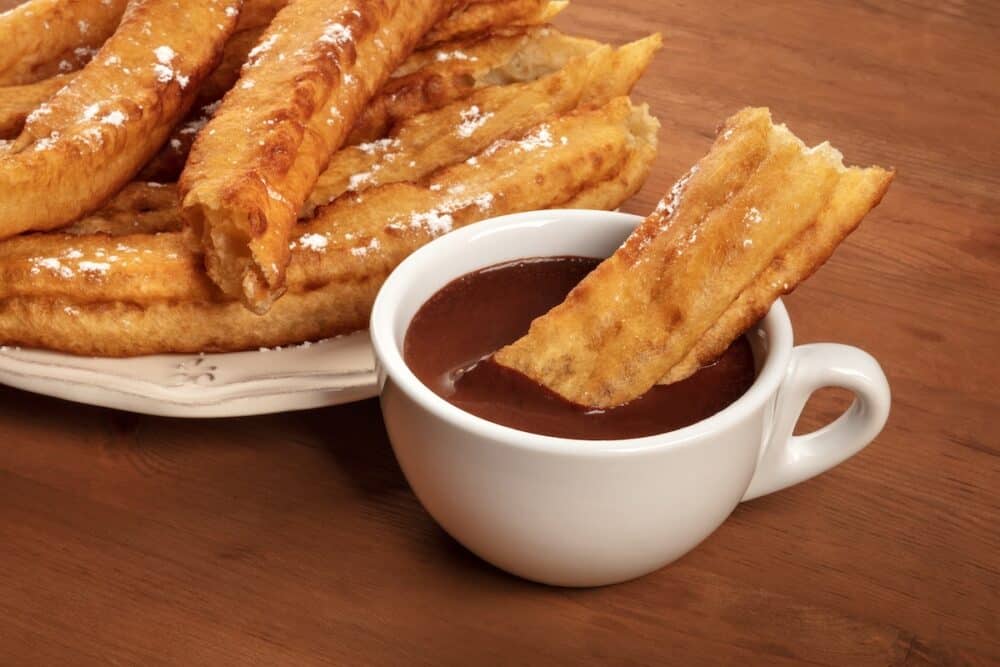 Traditional Spanish porras dipped in hot chocolate, a typical Madrid Sunday breakfast, on a dark rustic wooden background with copy space