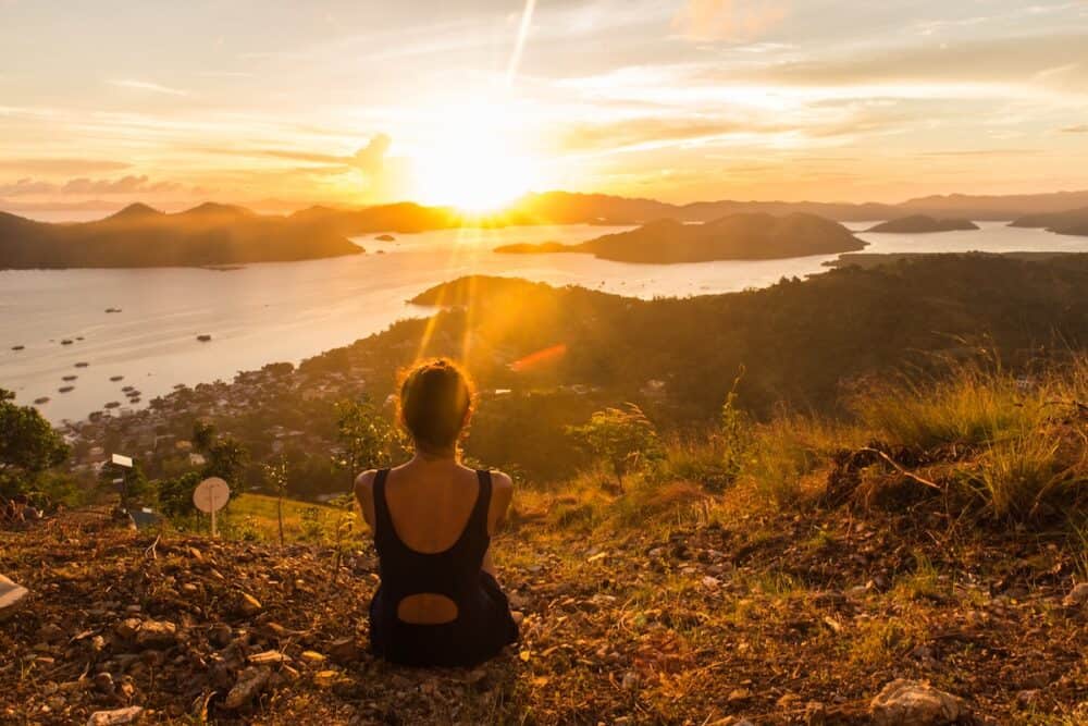 backview of girl, sitting on the earth and observing sunset in Coron city view point with sea and sky on the background in Philippines, Palawan
