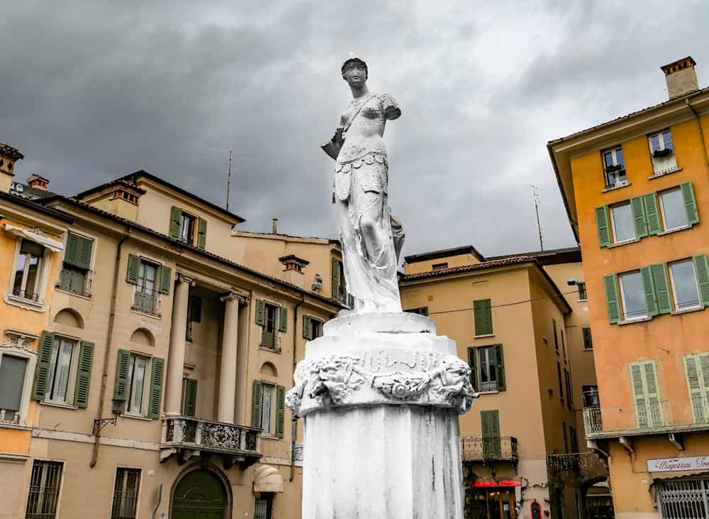 A classic statue amidst old architecture in Brescia, Italy, under a dramatic cloudy sky.