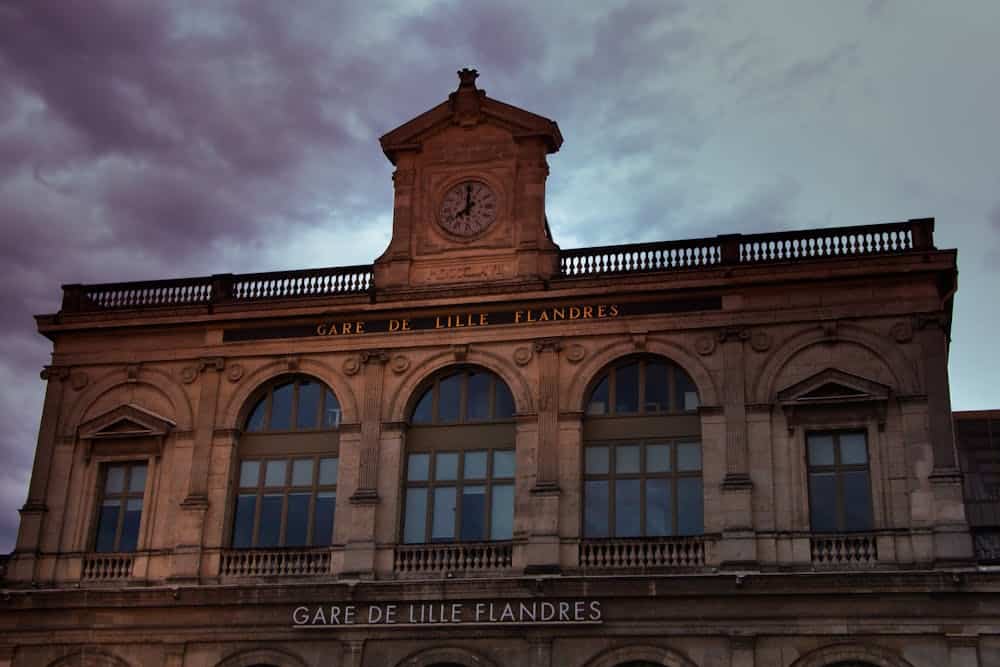 Majestic view of Gare de Lille Flandres clock tower under a dramatic sky.